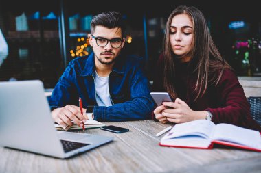 Onun iş arkadaşı onu arkadaş proje üzerinde çalışmak için mobil kullanmayı durdurmak için bekleyen hipster adam görmezden telefonu üzerinden sosyal ağlar sohbet ederken kamera arayan genç ciddi erkek öğrenci