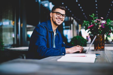 Hipster adam bloglama sosyal ağlar takipçileri ile online sohbet gülümseyen uzak iş yayını için dizüstü bilgisayarda metin yazarak Eyewear neşeli erkek metin yazarı portresi memnun