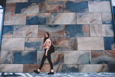 Tam uzunlukta portre çekici kadın Gezgin yürüyüş geçen duvar promosyon arka plan, modaya uygun kıyafet açık havada sırt çantası ile gezinme kamera bakarak giymiş güzel hippi kız