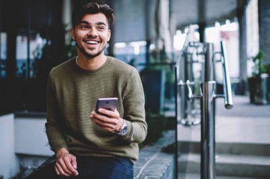 Mutlu sakallı hippi adam heyecanlı iyi haber alan Mesaj Kentsel ayarları üzerinde oturan Smartphone ile neşeli yakışıklı adam telefonda Sohbet mesajları ve aramalar için telefon tarifeler ile karşılar