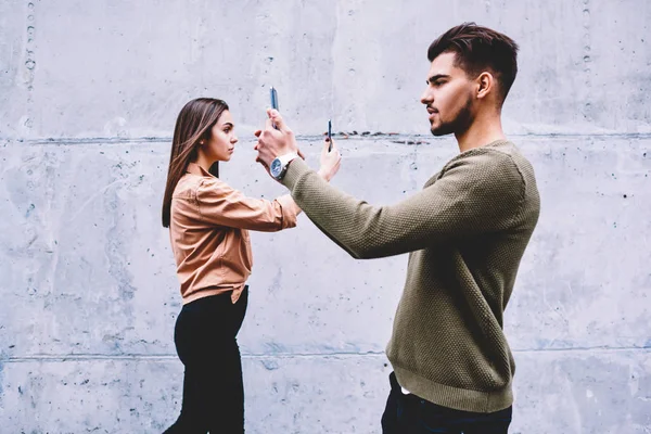 Young hipsters looking at modern smartphones living with internet addiction ignoring real-life communication, male and female friends taking selfie for networks concentrated on online popularity