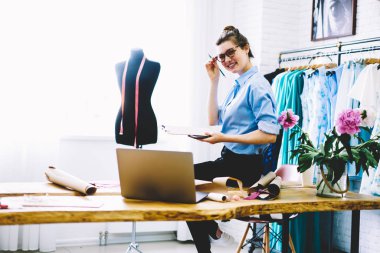 Terzi şık gözlük el üstünde okul sırası ile ekipman moda Studio arka plan üzerinde siyah manken ve trendy giyim koleksiyonu ile oturan önlemler için klasör holding olarak portresi