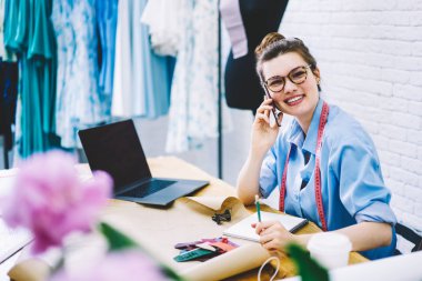 Neşeli modacı hakkında yeni üretim cep üzerinde söz yarım uzunluk portre şık giyim koleksiyonu ile memnun. Gülümseyen tasarımcı planlama kumaş kıyafeti fikirler cep telefonunda tartışıyor