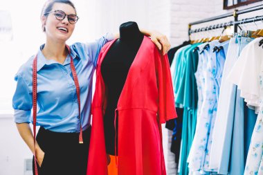 Neşeli başarılı terzi gözlük ve teyp için yarım uzunluk portre ayakta kendi şık showroom gelecekteki trendy elbise için pembe Tekstil malzeme ile siyah manken yakınındaki ölçer