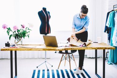 Masaüstü dizüstü aygıtı ve kesme tasarım kroki gelecekteki trendy koleksiyonu kendi şık showroom için yeni giysiler dikiş üzerinde çalışma ile ayakta optik gözlük içinde konsantre terzi