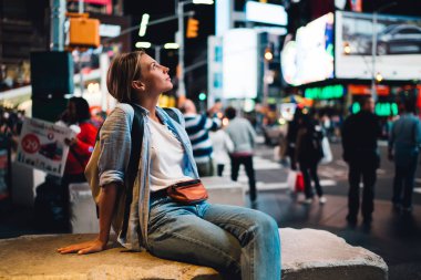 Modern mimarisi ile neon commercia parlayan ünlü New York landmark bakarak düşünceli hippi kız kalabalık sokakta oturan genç kadın Gezgin Time square ile hayran ışıklar