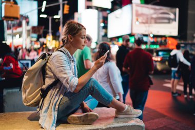 Genç kadın kadın Gezgin kalabalık Times Square'de akşam oturan smartphone üzerinden blog resimleri ilanıyla New York'a yolculuk sırasında dolaşım Internet kullanarak cep telefonunda mesaj okuma 