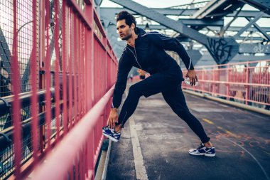 Yakışıklı genç modern şehrin köprüde sabah egzersiz sırasında spor egzersizleri yapıyor şık eşofman giymiş. Sportif jogger eğitim açık havada. Kentsel ortamda egzersiz sahip atletik erkek