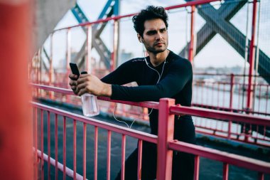 Sakallı uygun yakışıklı spor uzakta açık havada spor eğitim molası sırasında seyir kulaklık dinleme müzik hayranı. Smartphoe ve botte elinde tutan eşofman giymiş motive erkek atlet
