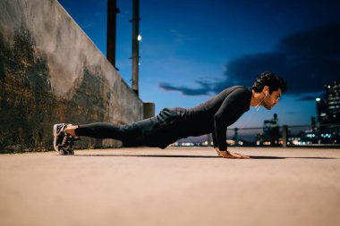 Genç motive adam yerden kentsel ortamda akşam egzersiz sırasında iterek spor. Uygun adam açık havada alacakaranlık şehir arka plan üzerinde spor vücut korumak için eğitim aktif giyim giyinmiş