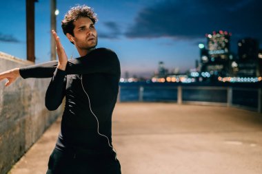Kentsel ortamda sıcak sırasında el spor egzersizleri yapıyor siyah aktif giyim profesyonel genç atlet giymiş. Motive sporcu yaşayan akşam egzersiz sırasında germe yapıyor