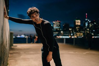 Yorgun uygun adam tatilinde zor akşam egzersiz sonrasında duvara yaslanmış kulaklık ses müzik dinleme eşofman giymiş. Etkin aşınmaya erkek koşucu spor eğitim açık sonra bitkin