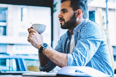 Ciddi genç adam için online iş fikri üzerine kahve molası sırasında düşünceli erkek onun Kupası serbest zaman çalışma alanı office coworking içinde dizüstü bilgisayar ile oturup üzerinde tutarak geliştirici konsantre oldum