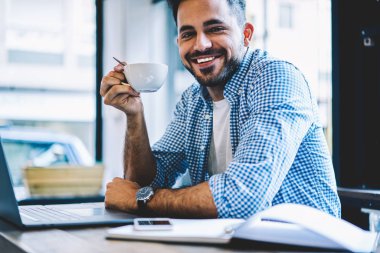 Ağ dizüstü bilgisayarda kahve, yetenekli gülümseyen freelancer holding Kupası online iş projesi başarıyla tamamladıktan sonra içme sırasında mola zevk neşeli erkek öğrenci portresi