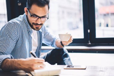 Akıllı erkek öğrenci kafeteryasında Not Defteri'nde yazma ödev görev yapmayı konsantre, yetenekli grafik tasarımcı çizim eskiz pencere yakınındaki kafede oturan zevk yaratıcı uzak iş