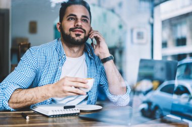 Ara kafe, erkek freelancer iş ayrıntıları ile teknoloji kafeteryada kahve içme otururken telefon konuşma sırasında tartışırken üzerinde cep telefonu konuşmayı dalgın genç adam