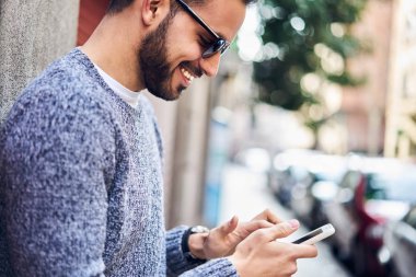 Komik resimler şehir sokak üzerinde duran smartphone üzerinden ağ ile ilgilenen hipster adam gülümsüyor, neşeli genç adam cep telefonu açık havada üzerinde rezervasyon uygulaması ile memnun kazanmaktan memnun