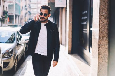 Genç erkek Smartphone'da arkadaşla şehir sokak, yakışıklı hipster adam cep telefonu konuşmayı kentsel ayarları açık havada geçen güneş gözlüğü üzerinde yürürken konuşmak trendy giyinmiş