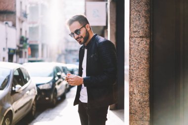 Hipster adam yolu ile kullanma smartphone cep telefonu ile şehir caddede yürüyüş arkadaşıyla Sohbet trendy giyim gülümseyen, neşeli yakışıklı erkek açık havada dosyalarını yükleyerek Internet bağlantısı ile memnun