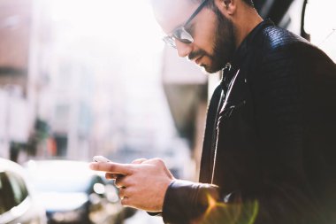 Web sayfasını kullanarak telefon açık havada arkadaşıyla Sohbet metin mesajları gönderme hipster biri sokak, kırpılmış görüntü üzerinde duran rezervasyon yapma smartphone üzerinden ağ dalgın yakışıklı erkek