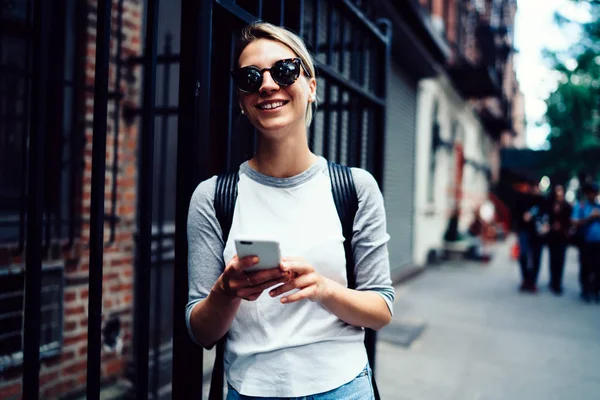 散歩余暇を楽しむスマート フォンを介して幸せな流行に敏感な女の子送信メッセージ サングラスの女性観光客に笑みを浮かべて移動観光その 中のオンライン チャットでのインターネット接続に満足してください — ストック写真