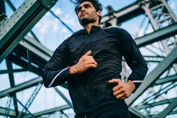 Below view of sportsman dressed in active wear for workout running at speed in urban setting.Motivated male jogger in active wear training outdoors on bridge for healthy vitality