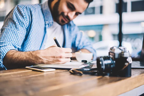 集中男学生写作业报告在笔记本上满意的创造性任务坐在桌面上 熟练的记者做笔记为文章花费时间在工作地点与设备 — 图库照片