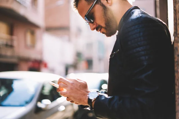 屋外で立っているハンサムな男性がインターネットに近代的な電話および 接続経由でマルチ メディア メッセージを送信するアプリケーションのカフェを検索するスマート フォンを使用して 流行に敏感な男の画像をトリミング — ストック写真