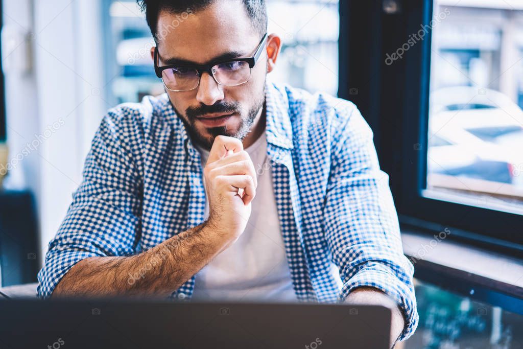 Pensive male it developer pondering solving problems with software on laptop computer reading information from networks,contemplative hipster guy checking banking account and making payment online