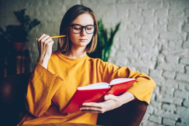 Dikkatle yaklaşan sınavına hazırlanması için edebiyat kitap okuma gözlük düşünceli akıllı öğrenci. Dalgın kadın, elinde kahve dükkanında oturmuş Not Defteri'nde yazılı eserin planı kontrol kalemi