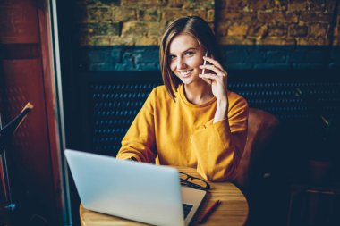 Yarım uzunluk portre dijital telefon netbook online veritabanı ile çalışan istemci ile konuşurken neşeli kadın Yöneticisi bağlı kablosuz 4 g için kameraya gülümseyen süre internet