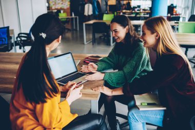 Neşeli öğrenciler teamworking ve boş ekran dijital dizüstü cihaz üzerindeki izlerken komik webinar. Başarılı pozitif kadın tasarımcılar ofisinde oturan netbook üzerinde online sunum tartışıyor