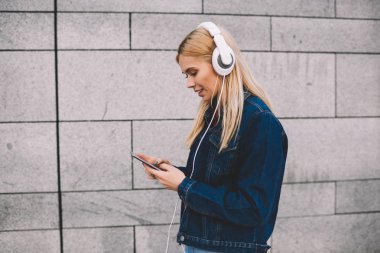 Hippi kız kot giyim gri promosyon arka plan yürüyüş modern Kulaklığımda dinlemek için smartphone cep telefonu ile müzik uygulamasında ses şarkı seçme giymiş yan görünüm