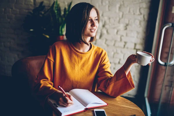 カフェの日記での目標のリストを行うに書く短い髪と思いやりのある若い女性 コーヒー飲料を楽しむ手帳にメモをしながら週末を夢見て幸せな女生徒 — ストック写真