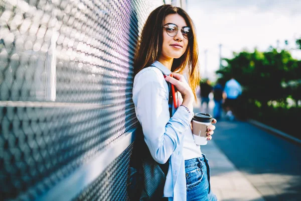 穿着休闲服装和眼镜的漂亮女孩的肖像在户外享受天气 积极的少女女时髦看着相机站在街上拿着最喜欢的咖啡去杯 — 图库照片