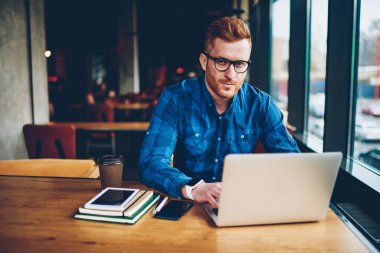Portre grafik tasarımcı ile Kızıl saçlı çalışma serbest dizüstü bilgisayar, kablosuz internet'e bağlı. Üniversitesi'nde oturan netbook üzerinde kurs için metni yazarak gözlük yetenekli öğrenci