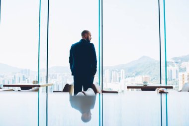 Arkadan görünüşü erkek girişimci giymiş şık giyim iş ortağı modern şık kafede cam pencerelerle beklerken pencereden dışarı bakıyor. Ofis binası içinde kendine güvenen gurur ceo