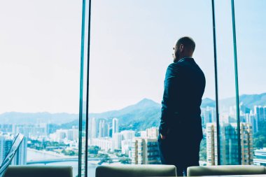 İşadamı kapalı ofis modern iç ayakta ve kendi şirket geliştirmek için yeni fikirler üzerinde düşünme resmi elbise giymiş. Windown dışında seyir ve metropolis sahne zevk gurur ceo