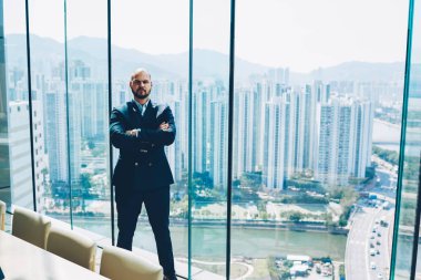 Kameraya bakarak şık elbiseli kendine güvenen erkek ntrepreneur tam uzunlukta portresi. Formal giyim ayakta yakınındaki cam pencere metropolis arka plan üzerinde ciddi yakışıklı icra müdürü giymiş
