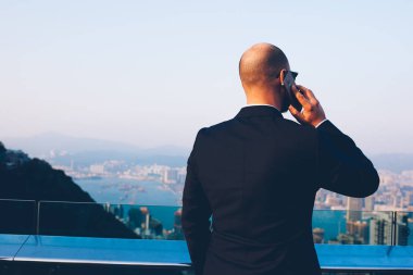 Arkadan görünüşü önemli iş konuşmayı meslektaşım yolu ile yüksek gökdelenler ile modern şehir güzel manzarayı smartphone aygıt ile siyah şık takım elbise giymiş erkek girişimci