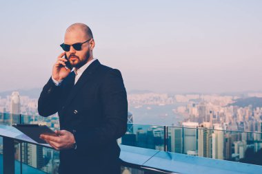 Meşgul emin iş adamı metropolis arka plan üzerinde kopya alanı yakınında duran dokunmatik yüzey üzerinde Web sitesinden okumak son finansal haberler sözünü smartphone meslektaşı ile konuşurken siyah güneş gözlüğü