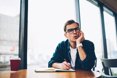 Yarım uzunluk portre yakışıklı hipster adam trendy Eyewear smartphone telefon konuşmayı şaşırttı. İçeride oturan genç adam modern üzerinde konuşurken kameraya bakan durulması telefon