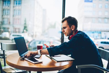 Akıllı erkek öğrenci ders projesi kafede için hazırlarken gözlük için daha iyi görüş alarak durulması. Yakışıklı hipster adam sahte ekranı ile dizüstü yanında masada oturan