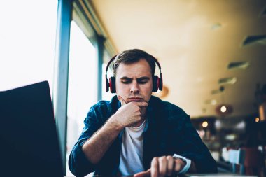 Genç yakışıklı durulması erkek öğrenci modern teknolojisi kafede oturan rekreasyon zevk trendy giyim giymiş. Boş vakit için online ders dinleme dalgın hipster adam