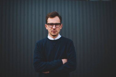 Genç yakışıklı erkek Blogger yarım uzunluk portre şık kıyafet ayakta duvara promosyon arka plan ile giyinmiş. Pozitif adam kameraya alan reklam yanında yürüyüş sırasında bakan