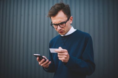 Yakışıklı düşünceli erkek blogger kontrol şık giysiler giymiş ziyaret kartı ve ağ arama bilgileri cep. Web sitesinde online rezervasyon ve ödeme hizmetini kullanarak yapma genç adam