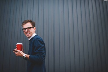 Yarım uzunluk portre yakışıklı erkek öğrenci ile modern cihaz ücretsiz vaktinizi gülümseyen ve lezzetli kahve götürün. Pozitif delikanlı iyi eğlenceler dururken Street alan reklam yakın