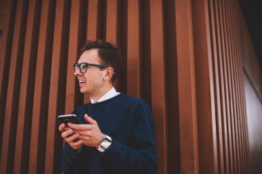 İyi görünümlü neşeli erkek öğrenci şık gözlük boş zaman açık havada becerikli alet ile harcama yaparken eğlenmek. Gülümseyen adam arkadaşlar açık havada yürüyüş sırasında cep telefonu kullanarak komik iletiler göndermesi