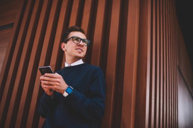 Pozitif delikanlı modern cihaz ve iyi bir ruh hali ile kentsel ayarda dinlenme zevk şık kıyafeti giymiş. Mutlu erkek kişi yaz Sokağı'nda eğlence ve sosyal ağ iletileri gönderme