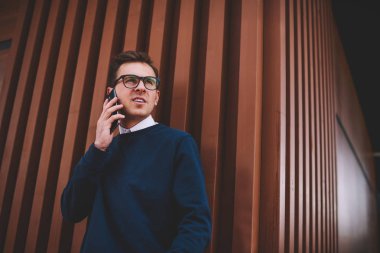 Yakışıklı olumlu erkek öğrenci şık Eyewear yaz telefonla konuşma sırasında sokak vasıl dinlenme zevk. Smartphone uygulama açık havada üzerinden mobil konuşmayı genç gülümseyen adam